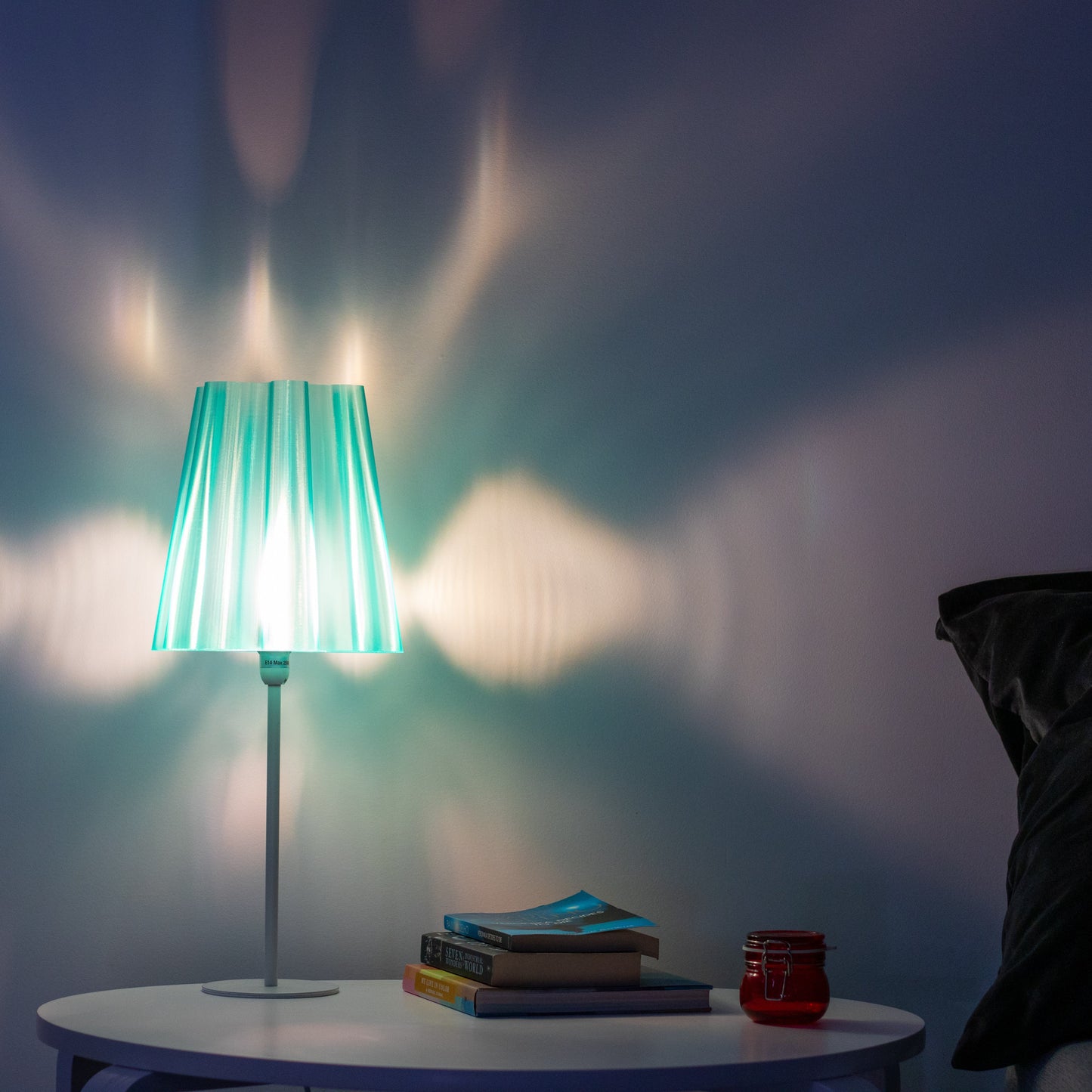 Translucent teal lamp shade with a warm white bulb, casting a beautiful light pattern on the wall, perfect for creating cozy ambiance. 3D printed lamp shades with semi-see through walls. 3D printed modern lamp shades.