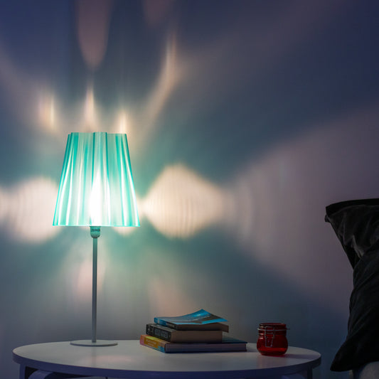 Translucent teal lamp shade with a warm white bulb, casting a beautiful light pattern on the wall, perfect for creating cozy ambiance. 3D printed lamp shades with semi-see through walls. 3D printed modern lamp shades.