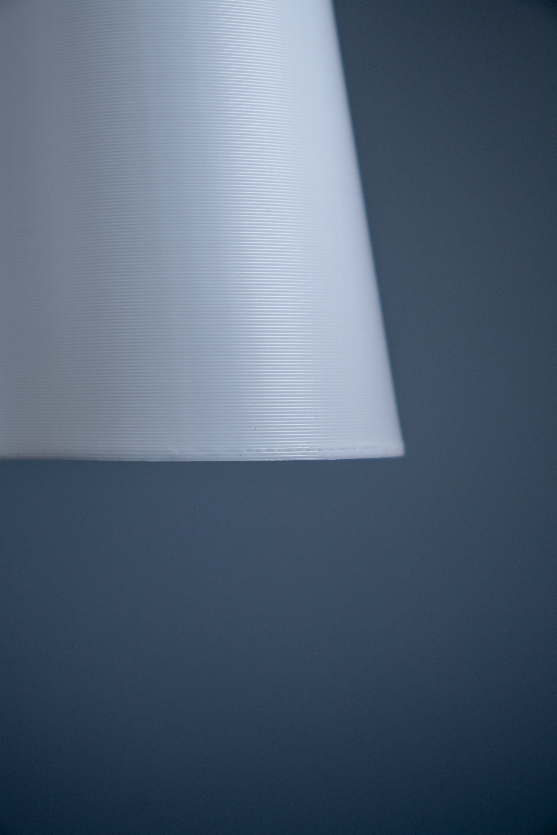 The image shows the beautiful layer lines of how the lamp shade is manufactured. The layer lines left by 3D printing manufacturing adds a texture which is very subtly aesthetic.