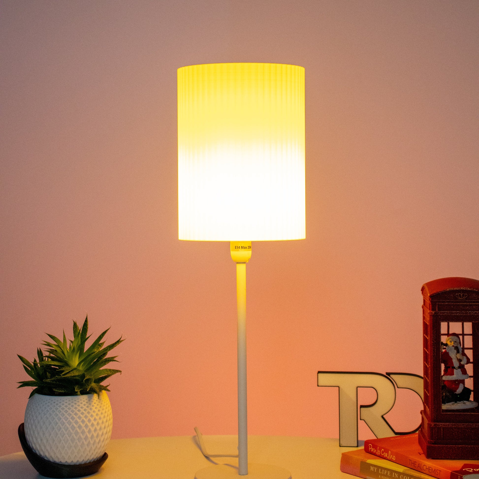 Minimalist lamp with a warm white cylindrical shade, placed on a table with decor items including a succulent and books, creating a cozy vibe.Perfect for study table. Great for bedside table. 3D printed lampshade in yellow colour.